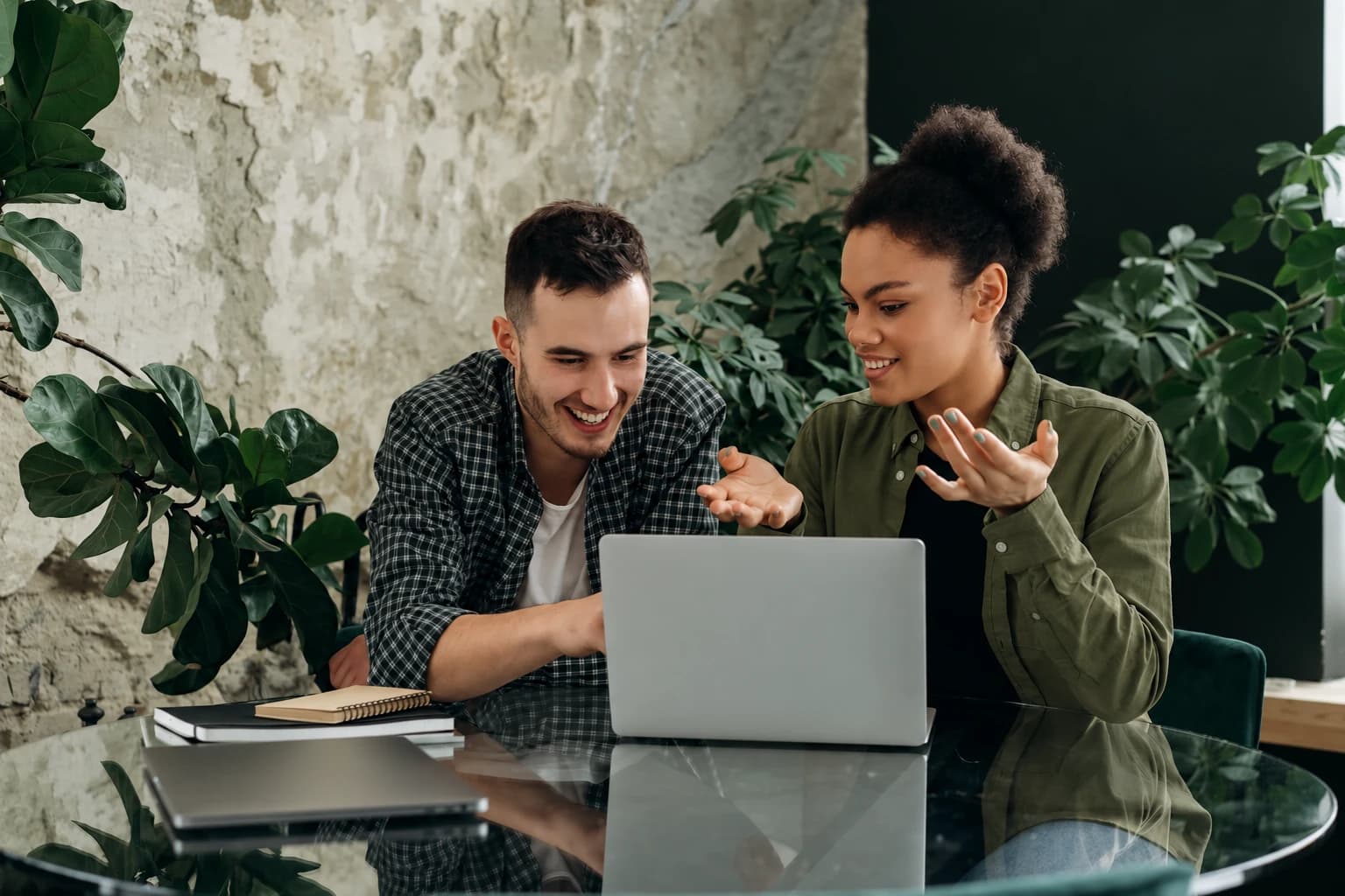 Two colleagues discussing work on a laptop in a plant-filled workspace
